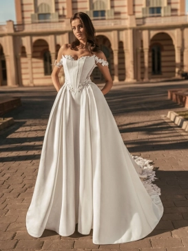 Blue by Enzoani Udell is a luxury satin ballgown wedding dress featuring a structured corset-inspired bodice, romantic off-the-shoulder straps, delicate floral appliqué detailing and a dramatic cathedral-length train. Designed for modern brides seeking a s