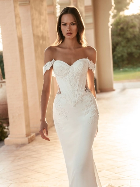 Blue by Enzoani Umani is a luxury fitted mermaid wedding dress featuring a romantic off-the-shoulder neckline, sculpted corset-inspired bodice, illusion side detailing and delicate floral lace appliqués. Designed for brides seeking a sophisticated designer