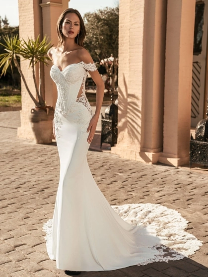Blue by Enzoani Umani is a luxury fitted mermaid wedding dress featuring a romantic off-the-shoulder neckline, sculpted corset-inspired bodice, illusion side detailing and delicate floral lace appliqués. Designed for brides seeking a sophisticated designer