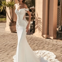 Blue by Enzoani Umani is a luxury fitted mermaid wedding dress featuring a romantic off-the-shoulder neckline, sculpted corset-inspired bodice, illusion side detailing and delicate floral lace appliqués. Designed for brides seeking a sophisticated designer