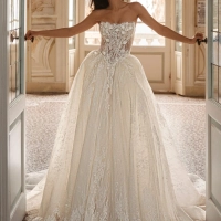 Enzoani Waylen luxury wedding dress with a strapless sweetheart neckline, intricately embroidered floral lace corset bodice, voluminous ball gown skirt, couture detailing, and dramatic cathedral train. Designer bridal gown by Enzoani combining modern roman