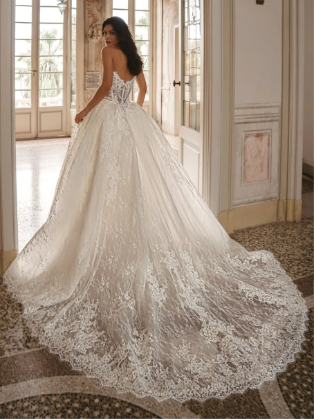 Enzoani Waylen luxury wedding dress with a strapless sweetheart neckline, intricately embroidered floral lace corset bodice, voluminous ball gown skirt, couture detailing, and dramatic cathedral train. Designer bridal gown by Enzoani combining modern roman
