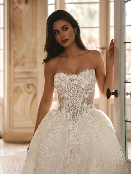 Enzoani Waylen luxury wedding dress with a strapless sweetheart neckline, intricately embroidered floral lace corset bodice, voluminous ball gown skirt, couture detailing, and dramatic cathedral train. Designer bridal gown by Enzoani combining modern roman