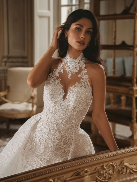 Enzoani Wednesday luxury wedding dress with a fitted mermaid silhouette, illusion halter neckline, floral lace embroidery, sculpted corset bodice, detachable overskirt, and dramatic cathedral train. Couture bridal gown by Enzoani combining modern glamour,