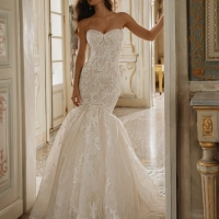 Enzoani Willa wedding dress. A luxury strapless mermaid bridal gown featuring a structured sweetheart neckline bodice adorned with intricate floral lace appliqués and subtle beadwork. The fitted silhouette hugs the hips before flaring into a dramatic lace