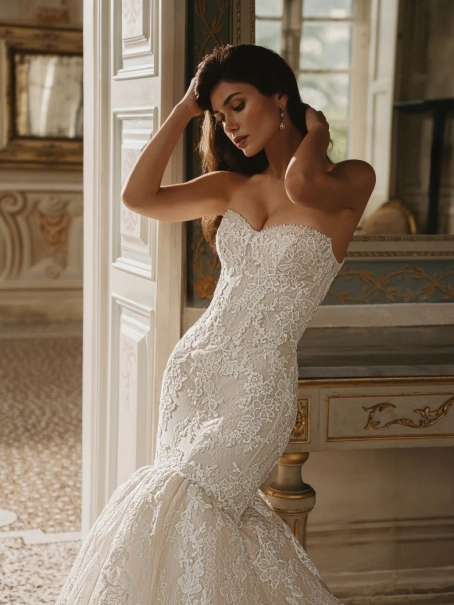 Enzoani Willa wedding dress. A luxury strapless mermaid bridal gown featuring a structured sweetheart neckline bodice adorned with intricate floral lace appliqués and subtle beadwork. The fitted silhouette hugs the hips before flaring into a dramatic lace