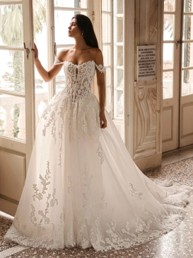 Enzoani Winona is a luxury ballgown wedding dress featuring an illusion corset bodice, romantic off-the-shoulder straps, intricate floral lace appliqué and a dramatic cathedral-length train. Designed for brides seeking a princess wedding dress with couture