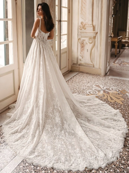 Enzoani Winslow is a luxury A-line wedding dress featuring intricate floral lace embroidery, a softly structured bodice, elegant shoulder straps and a graceful cathedral-length train. Designed for brides seeking a timeless designer wedding gown that blends