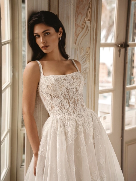Enzoani Winslow is a luxury A-line wedding dress featuring intricate floral lace embroidery, a softly structured bodice, elegant shoulder straps and a graceful cathedral-length train. Designed for brides seeking a timeless designer wedding gown that blends