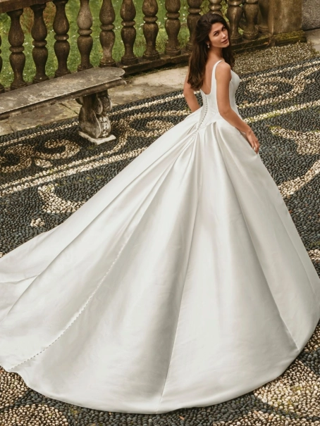 Enzoani Wisteria is a luxury satin ballgown wedding dress featuring a structured corset-inspired bodice, elegant scoop neckline, wide shoulder straps and dramatic architectural draping. Designed for brides seeking a minimalist designer wedding gown with ti
