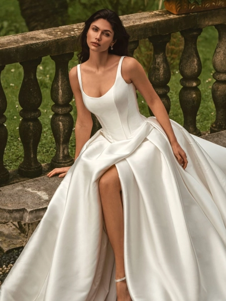 Enzoani Wisteria is a luxury satin ballgown wedding dress featuring a structured corset-inspired bodice, elegant scoop neckline, wide shoulder straps and dramatic architectural draping. Designed for brides seeking a minimalist designer wedding gown with ti