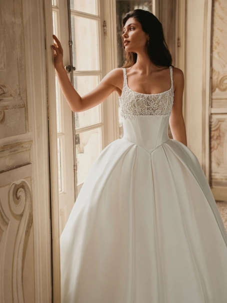 Enzoani Wren is a luxury satin ballgown wedding dress featuring a delicately embroidered lace bodice, elegant square neckline, supportive shoulder straps and a dramatic cathedral-length train. Designed for brides seeking a timeless designer wedding gown th