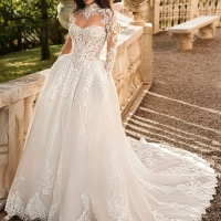 Enzoani Wynn is a luxury princess ballgown wedding dress featuring a high illusion neckline, long lace sleeves, structured corset bodice and intricate embroidered lace detailing throughout. Designed for brides seeking a regal designer wedding gown with cou