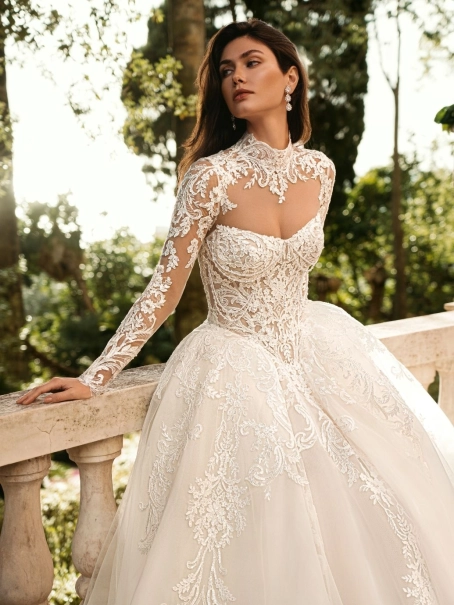 Enzoani Wynn is a luxury princess ballgown wedding dress featuring a high illusion neckline, long lace sleeves, structured corset bodice and intricate embroidered lace detailing throughout. Designed for brides seeking a regal designer wedding gown with cou