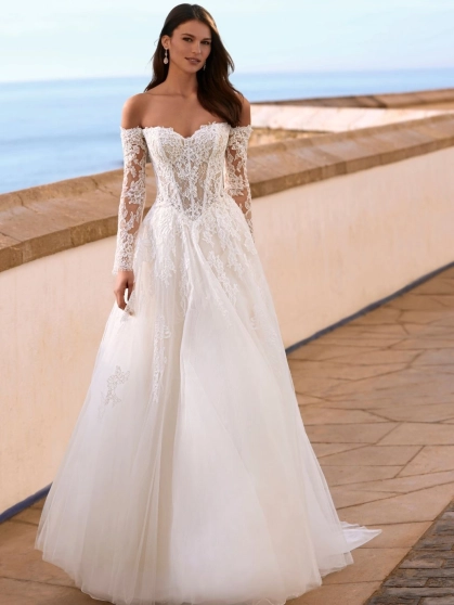 Love Faiza is a romantic A-line wedding dress from the 2027 collection featuring an illusion lace corset bodice, detachable off-the-shoulder long lace sleeves and a flowing soft tulle skirt with floral lace appliqués. Designed by Enzoani for brides seeking
