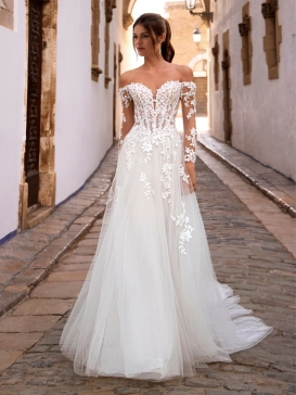 Love by Enzoani FISELLE is a romantic A-line wedding dress featuring a sheer illusion corset bodice adorned with dimensional floral lace appliqués that cascade into a soft layered tulle skirt. The gown is completed with detachable off-the-shoulder illusion