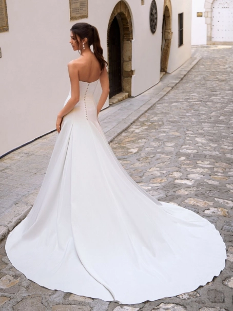 Love by Enzoani FLORENZA is a sophisticated fit and flare wedding dress crafted from luxurious satin with clean, sculptural lines. The gown features an elegant attached draped off-the-shoulder shawl, complemented by sheer illusion floral lace long sleeves