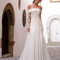 Love by Enzoani FLORENZA is a sophisticated fit and flare wedding dress crafted from luxurious satin with clean, sculptural lines. The gown features an elegant attached draped off-the-shoulder shawl, complemented by sheer illusion floral lace long sleeves