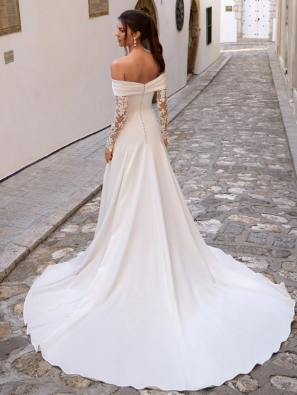 Love by Enzoani FLORENZA is a sophisticated fit and flare wedding dress crafted from luxurious satin with clean, sculptural lines. The gown features an elegant attached draped off-the-shoulder shawl, complemented by sheer illusion floral lace long sleeves