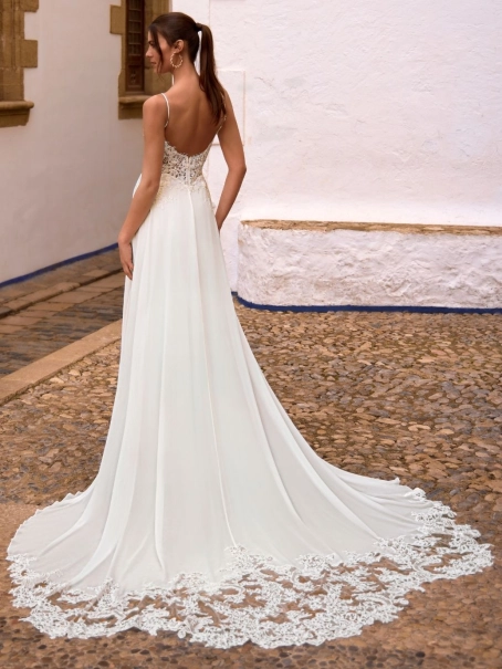 Love by Enzoani FLORETTA is an effortlessly romantic fit and flare wedding dress featuring a sheer illusion bodice adorned with intricate floral lace appliqués and delicate spaghetti straps. Soft illusion side panels create a flattering, sculpted silhouett