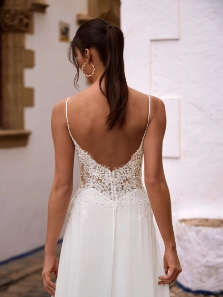 Love by Enzoani FLORETTA is an effortlessly romantic fit and flare wedding dress featuring a sheer illusion bodice adorned with intricate floral lace appliqués and delicate spaghetti straps. Soft illusion side panels create a flattering, sculpted silhouett