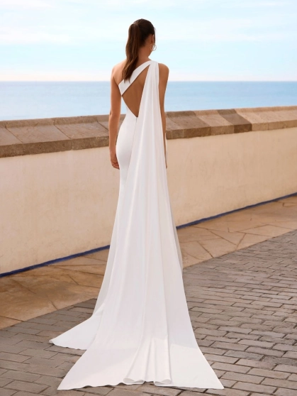 Love by Enzoani FLYNNE is a contemporary minimalist wedding dress crafted in luxurious crepe. This elegant fit and flare silhouette features a softly draped one-shoulder neckline, figure-enhancing ruching across the bodice, and a striking open back framed