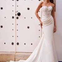 Love by Enzoani FOSIRA is a glamorous fit and flare wedding dress that combines a sparkling beaded illusion corset bodice with luxurious crepe. Featuring a romantic sweetheart neckline, exposed corset boning, intricate beadwork and soft draping across the