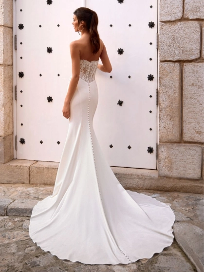 Love by Enzoani FOSIRA is a glamorous fit and flare wedding dress that combines a sparkling beaded illusion corset bodice with luxurious crepe. Featuring a romantic sweetheart neckline, exposed corset boning, intricate beadwork and soft draping across the