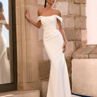 Love by Enzoani FRALISSE is a modern minimalist fit and flare wedding dress crafted with clean lines and timeless elegance. Featuring a softly draped off-the-shoulder neckline, flattering ruched bodice, sculpted silhouette and an open boned back bodice for