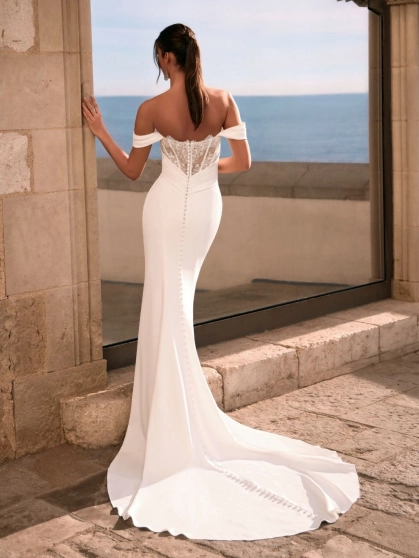 Love by Enzoani FRALISSE is a modern minimalist fit and flare wedding dress crafted with clean lines and timeless elegance. Featuring a softly draped off-the-shoulder neckline, flattering ruched bodice, sculpted silhouette and an open boned back bodice for