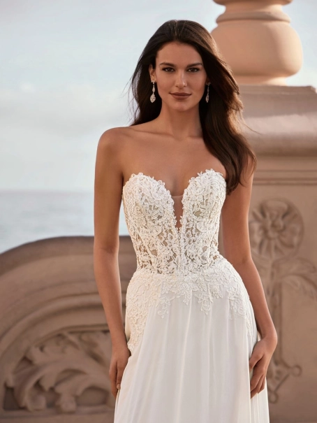 Love by Enzoani FRANCETTE is a romantic chiffon A-line wedding dress featuring an illusion lace corset bodice adorned with delicate floral lace appliqués, a plunging sweetheart neckline and a soft flowing chiffon skirt. Combining lightweight movement with