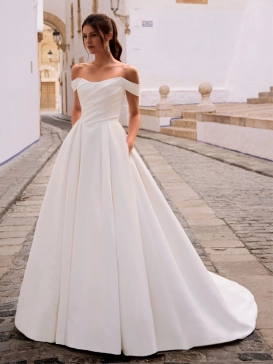 Love by Enzoani FRANCINA is a timeless satin ball gown wedding dress featuring a softly draped off-the-shoulder neckline, flattering ruched bodice and a full pleated skirt with hidden pockets. Combining classic bridal elegance with modern functionality, th