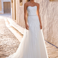 Love by Enzoani FRANCIS is a romantic A-line wedding dress featuring a strapless sweetheart neckline, floral lace appliqués cascading from the bodice into the skirt, a delicate beaded waistband and layers of soft tulle. Designed to create an effortlessly e