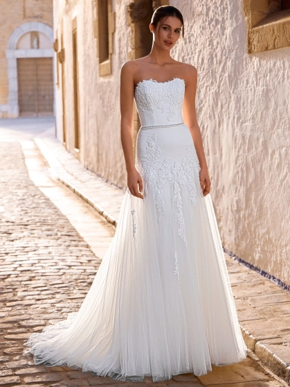 Love by Enzoani FRANCIS is a romantic A-line wedding dress featuring a strapless sweetheart neckline, floral lace appliqués cascading from the bodice into the skirt, a delicate beaded waistband and layers of soft tulle. Designed to create an effortlessly e