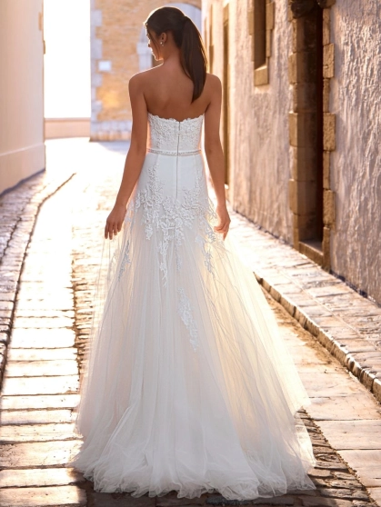 Love by Enzoani FRANCIS is a romantic A-line wedding dress featuring a strapless sweetheart neckline, floral lace appliqués cascading from the bodice into the skirt, a delicate beaded waistband and layers of soft tulle. Designed to create an effortlessly e