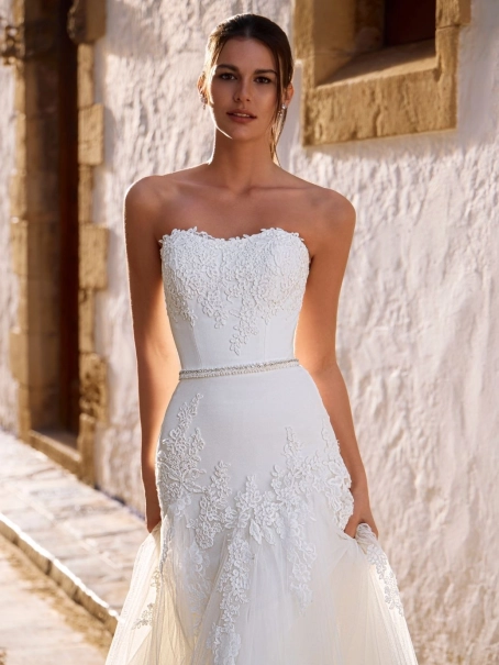 Love by Enzoani FRANCIS is a romantic A-line wedding dress featuring a strapless sweetheart neckline, floral lace appliqués cascading from the bodice into the skirt, a delicate beaded waistband and layers of soft tulle. Designed to create an effortlessly e