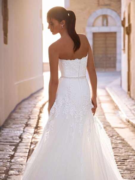 Love by Enzoani FRANCIS is a romantic A-line wedding dress featuring a strapless sweetheart neckline, floral lace appliqués cascading from the bodice into the skirt, a delicate beaded waistband and layers of soft tulle. Designed to create an effortlessly e