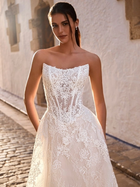 Love by Enzoani FRAVELLE is a romantic A-line wedding dress featuring a strapless sweetheart neckline, an illusion corset bodice with visible boning, intricate floral lace appliqués and a lightweight lace skirt with soft layers that create effortless movem