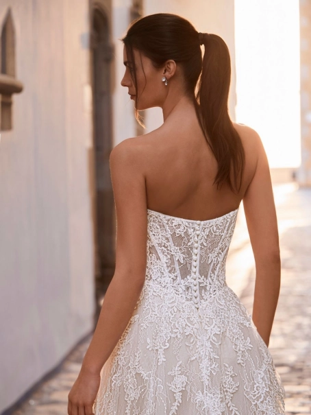 Love by Enzoani FRAVELLE is a romantic A-line wedding dress featuring a strapless sweetheart neckline, an illusion corset bodice with visible boning, intricate floral lace appliqués and a lightweight lace skirt with soft layers that create effortless movem