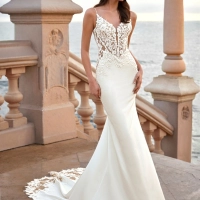 Love by Enzoani FRELYNN is a sophisticated fitted wedding dress featuring delicate spaghetti straps, an illusion corset bodice adorned with dimensional floral lace appliqués and exposed boning, paired with a sleek crepe mermaid skirt. The figure-enhancing