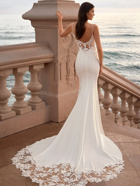 Love by Enzoani FRELYNN is a sophisticated fitted wedding dress featuring delicate spaghetti straps, an illusion corset bodice adorned with dimensional floral lace appliqués and exposed boning, paired with a sleek crepe mermaid skirt. The figure-enhancing